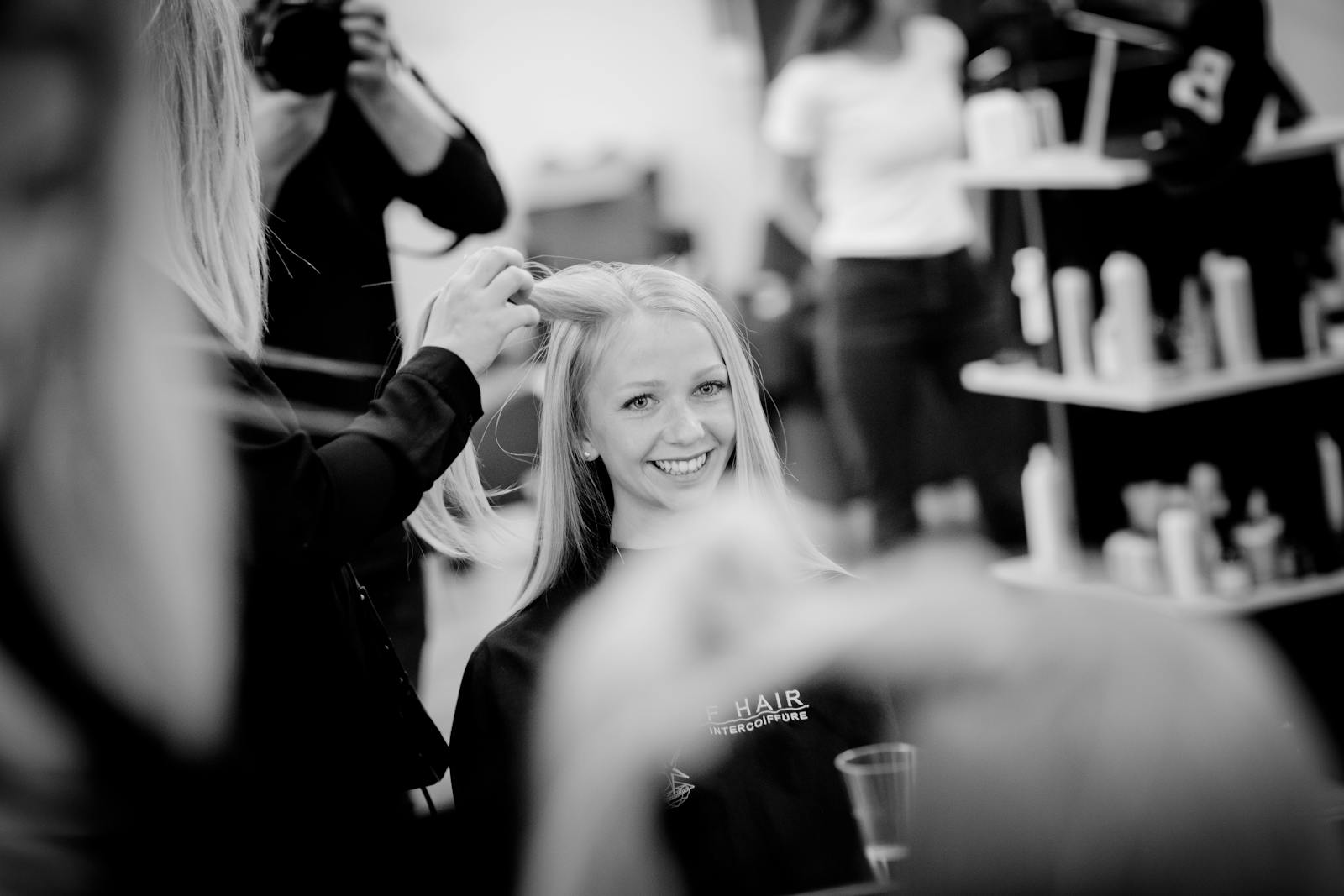 Smiling woman having her hair styled in a salon setting, captured in black and white.